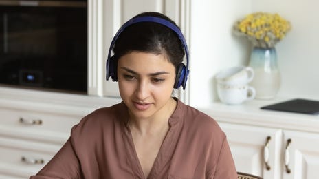 Woman in her kitchen with headphones talking to her instructor during an online intensive language lesson with Berlitz Canada