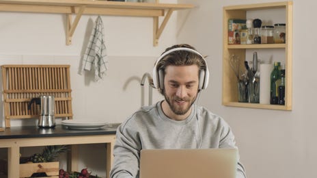 Man in headset sitting in his kitchen and taking an online English class with Berlitz Toronto from his laptop