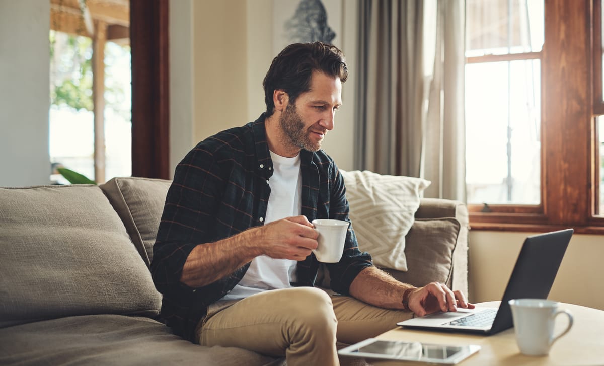Man holding a cup of tea and attending an online Spanish lesson in Winnipeg from his laptop