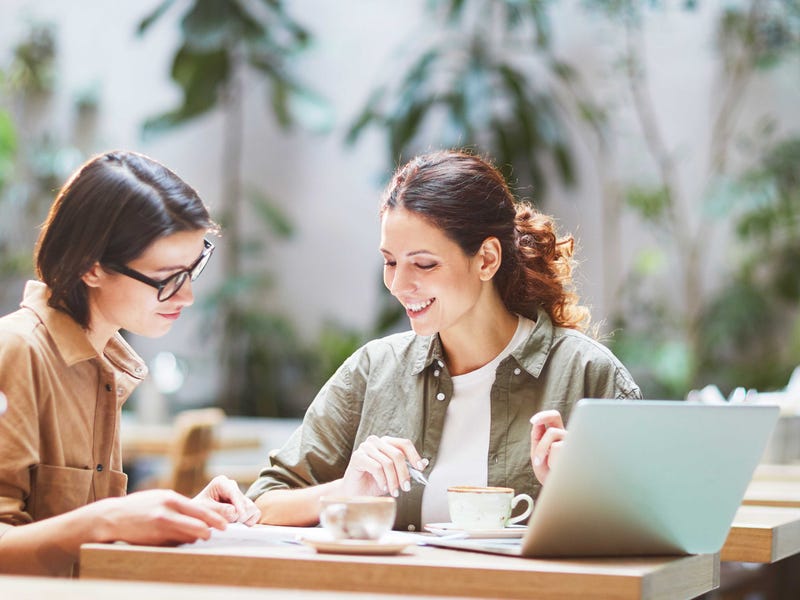 Woman teaching English abroad to another woman while sitting at a desk outside
