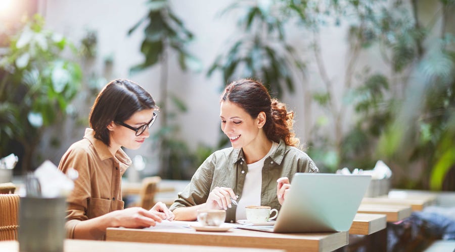 Woman teaching English abroad to another woman while sitting at a desk outside