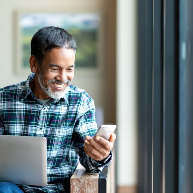 Man with a laptop checking out the Six-Week Challenge on his phone and smiling
