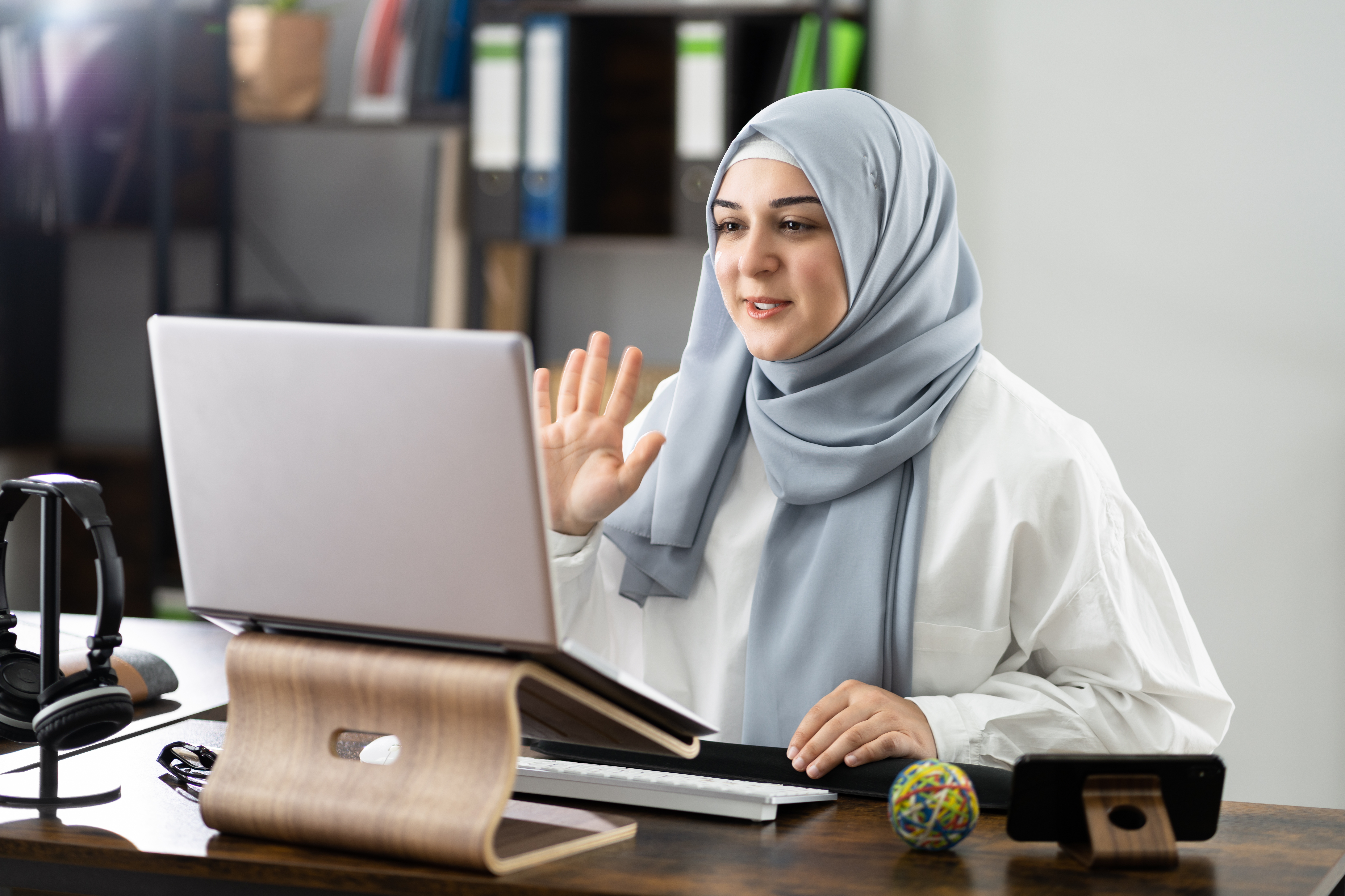 Woman in Edmonton sitting at her desk and waving at her instructor in the camera while she attends an online language lesson with Berlitz