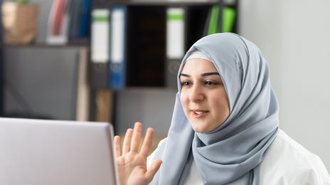 Woman in Edmonton sitting at her desk and waving at her instructor in the camera while she attends an online language lesson with Berlitz