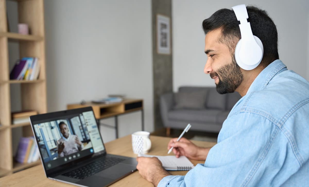 Man with headphones attending an online Spanish lesson with Berlitz Edmonton from his laptop and making notes