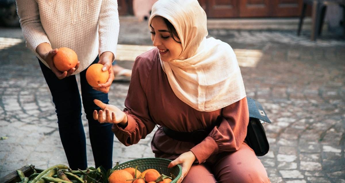 Woman in a scarf looking at oranges and saying yes to the seller