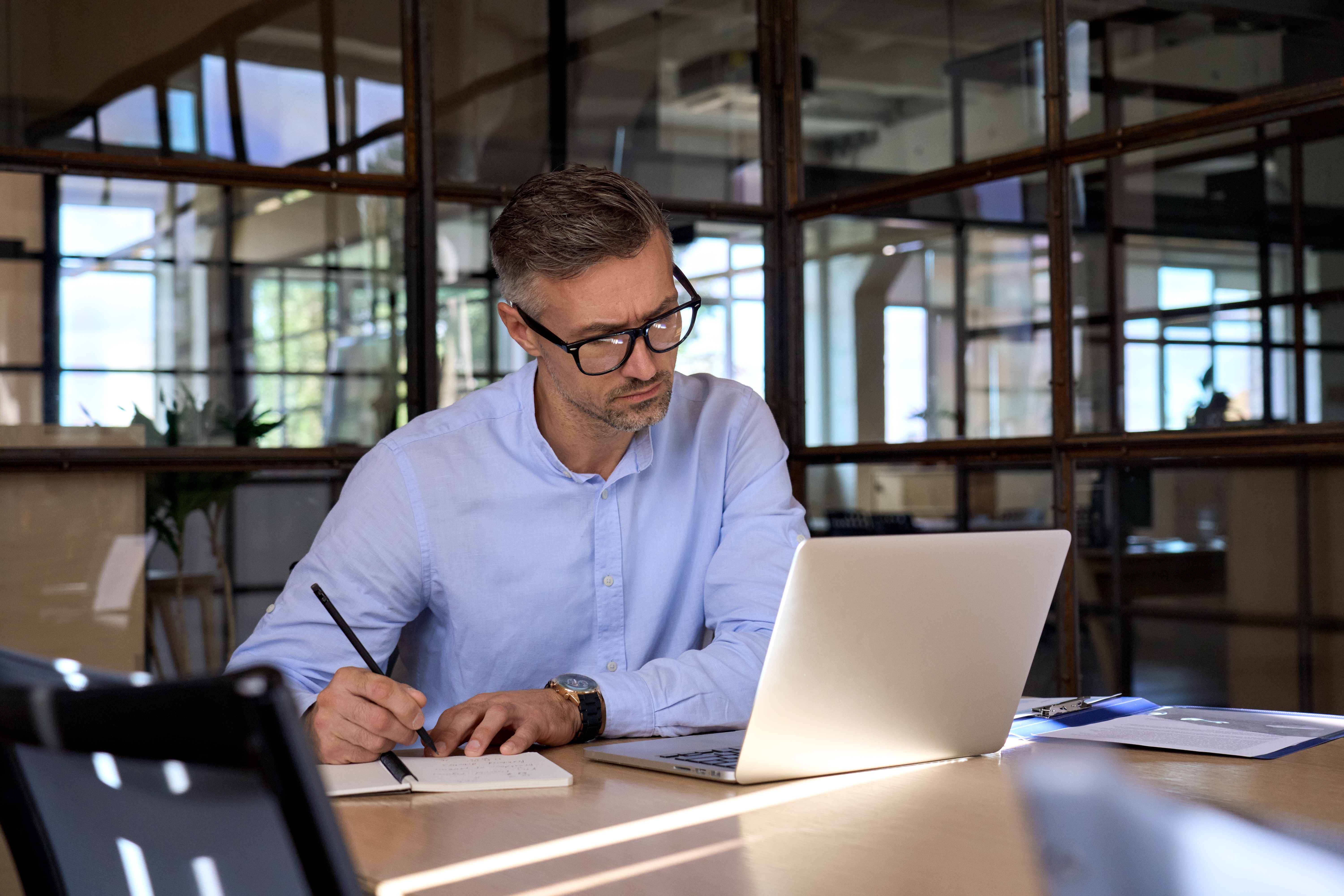 Man making notes while attending an online TEF preparation course with Berlitz Edmonton from his laptop in the office