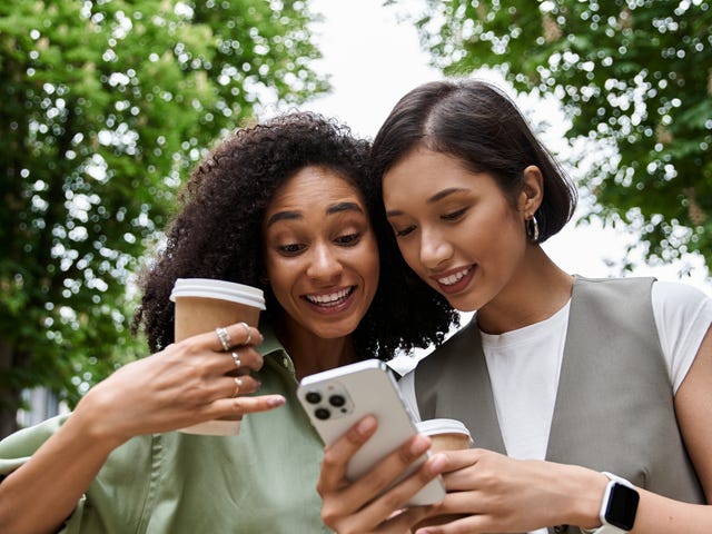 Two friends holding a phone and reading about online semi-private language classes with Berlitz while smiling