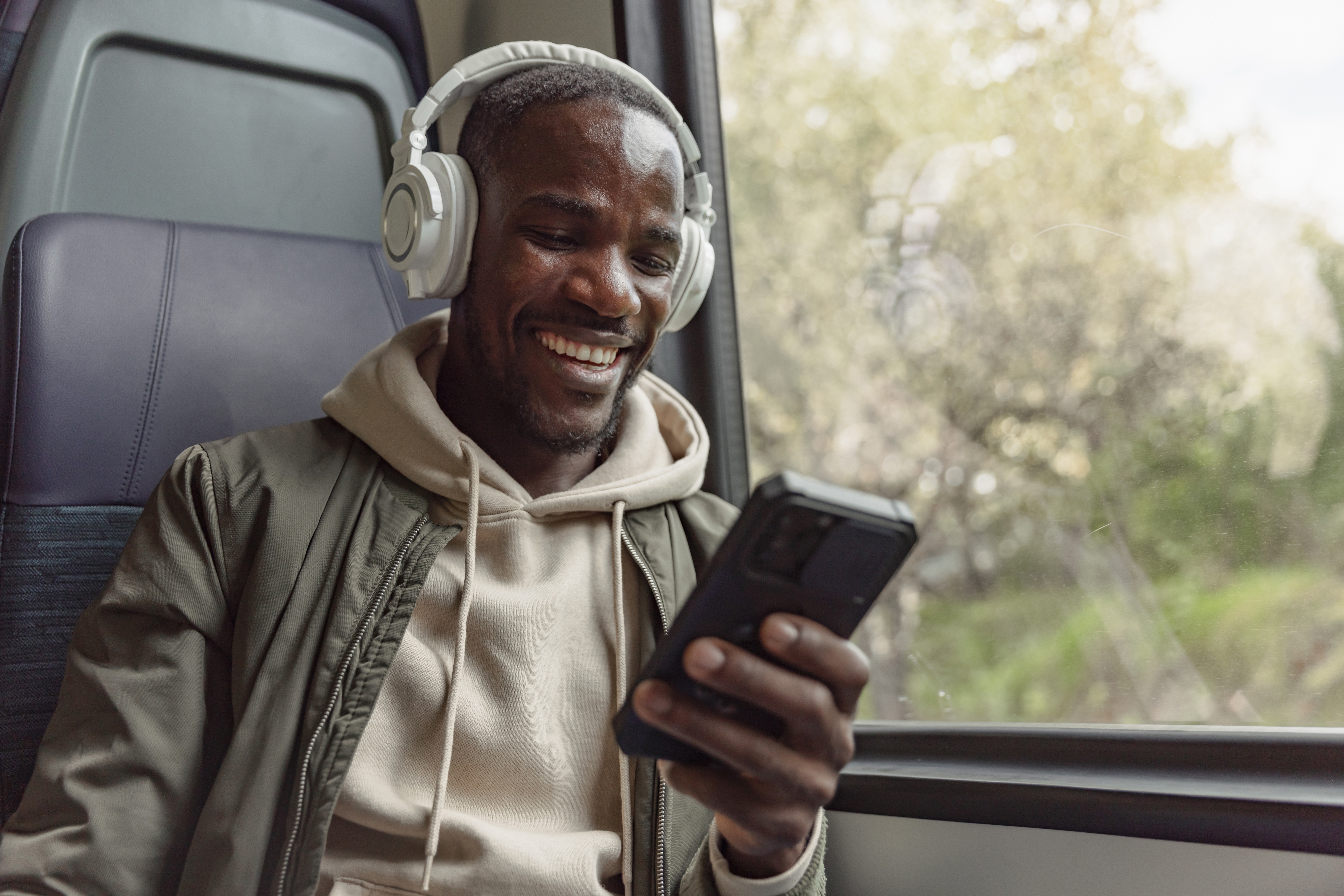 Man on the bus with headphones holding his phone and learning a language with Berlitz's self-study courses