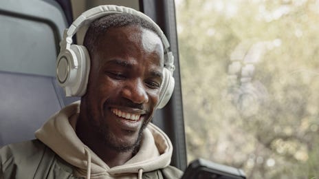 Man on the bus with headphones holding his phone and learning a language with Berlitz's self-study courses