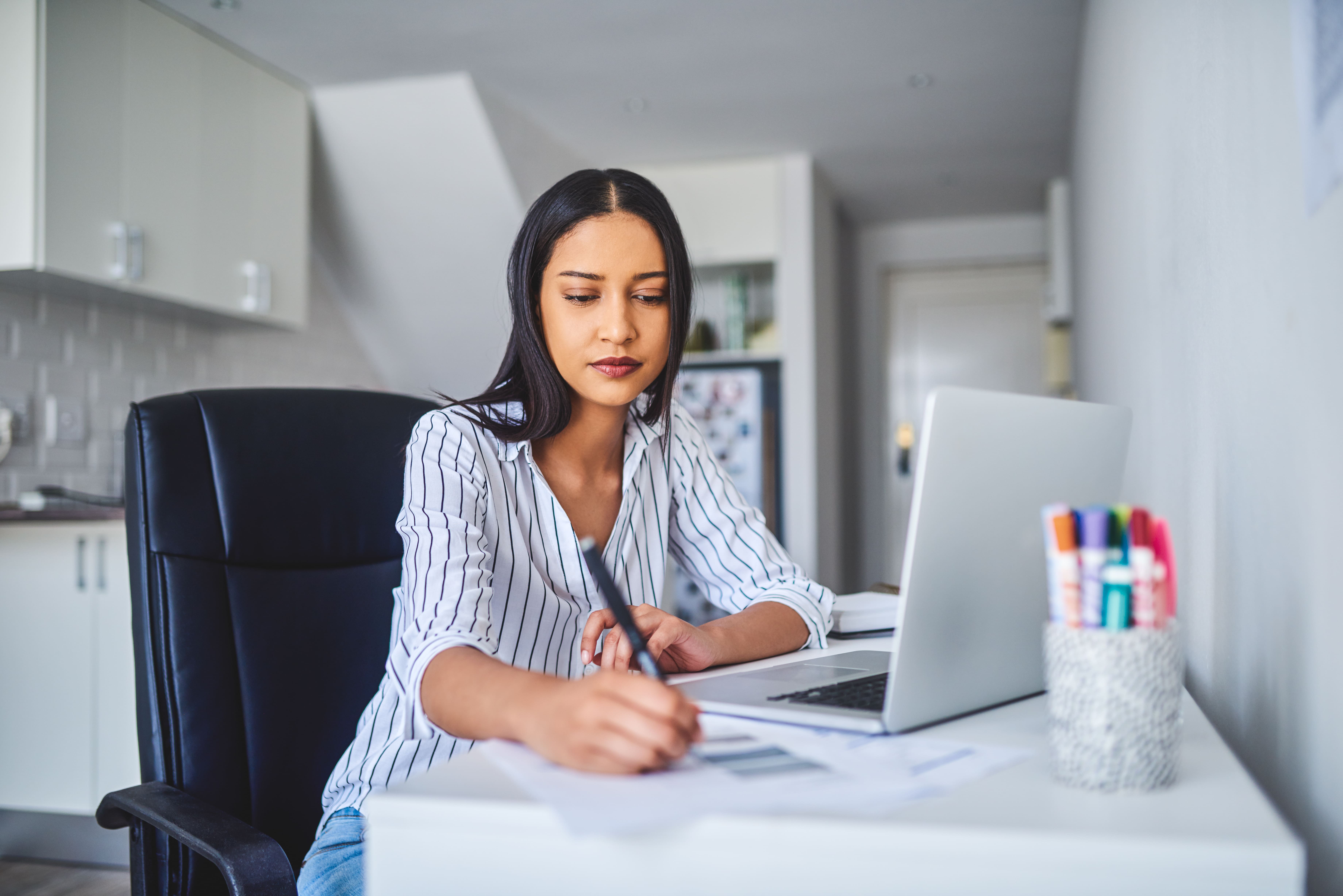 Woman in front of a laptop writing an essay in a notebook and preparing for her Test of Written Expression