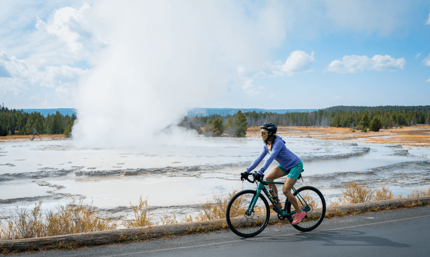 Hannah Eden rides a bike next to a geyser in Yellowstone National Park.