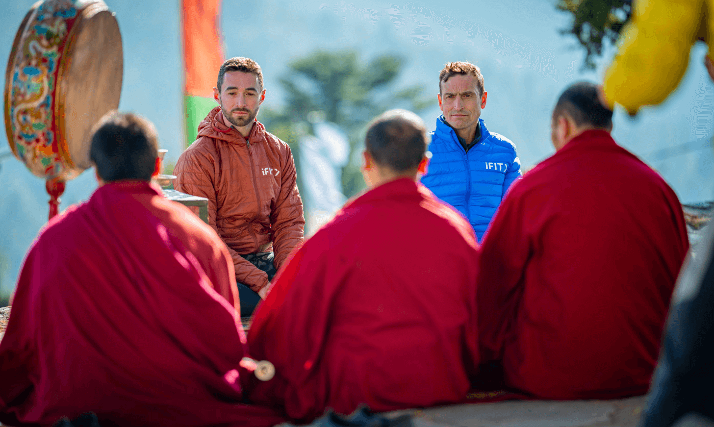 iFIT Trainer Casey Gilbert and iFIT Guide Kenton Cool sit with Buddhist monks in Bhutan.