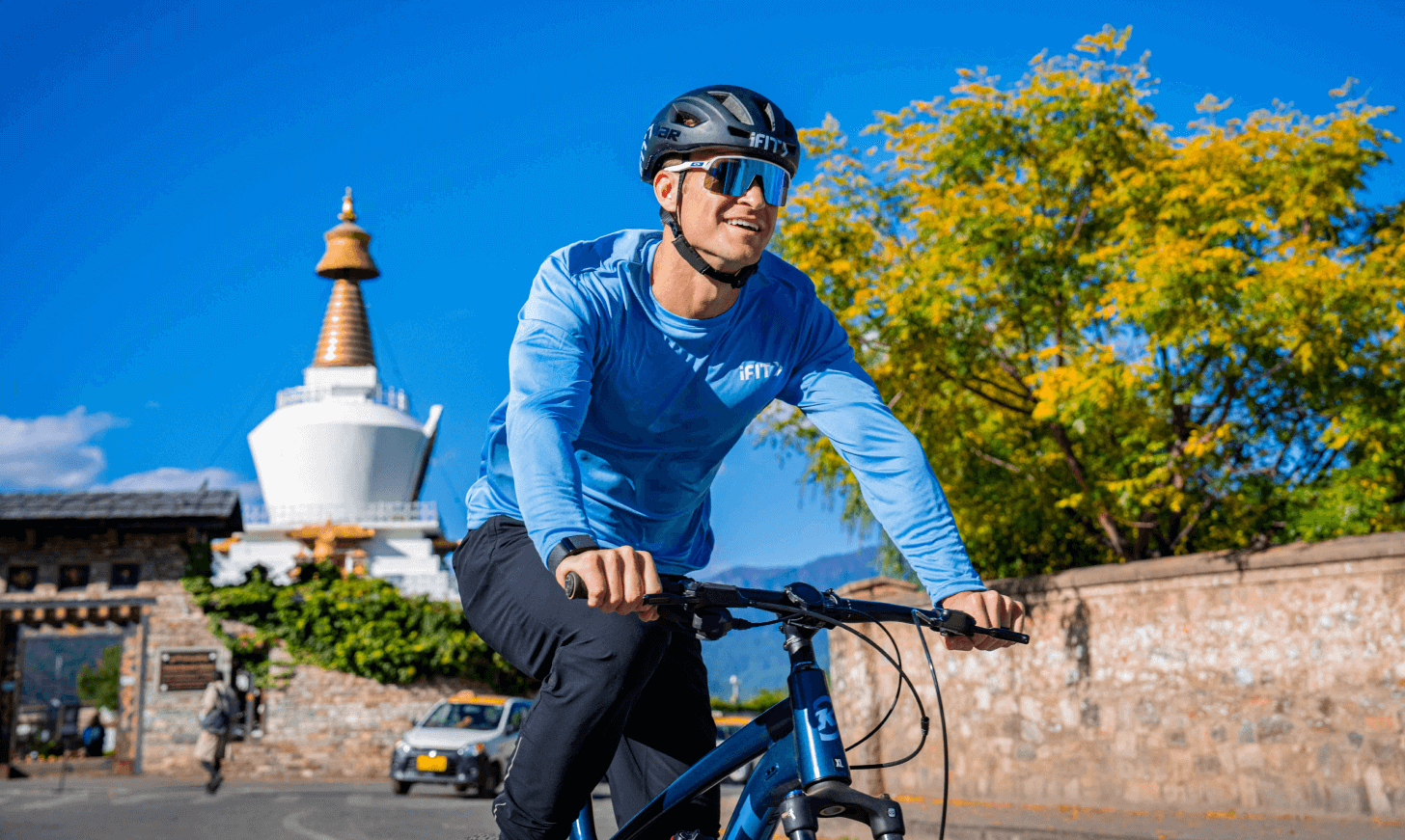 iFIT Trainer John Peel rides his bike past a white and gold monument in Bhutan.