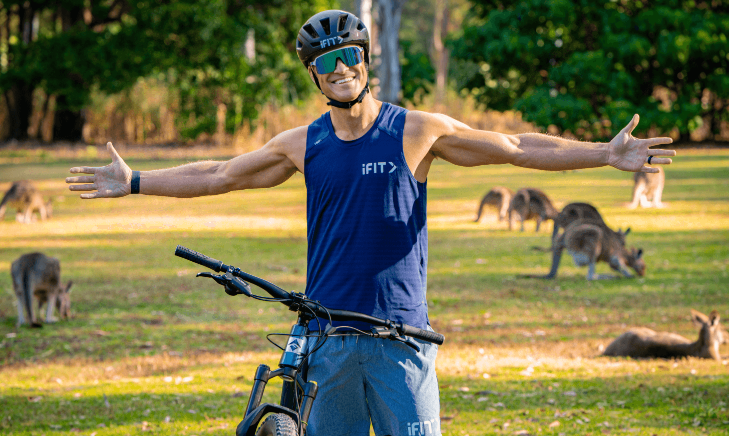 iFIT Trainer John Peel stands with his bike in front of a kangaroo-filled field.