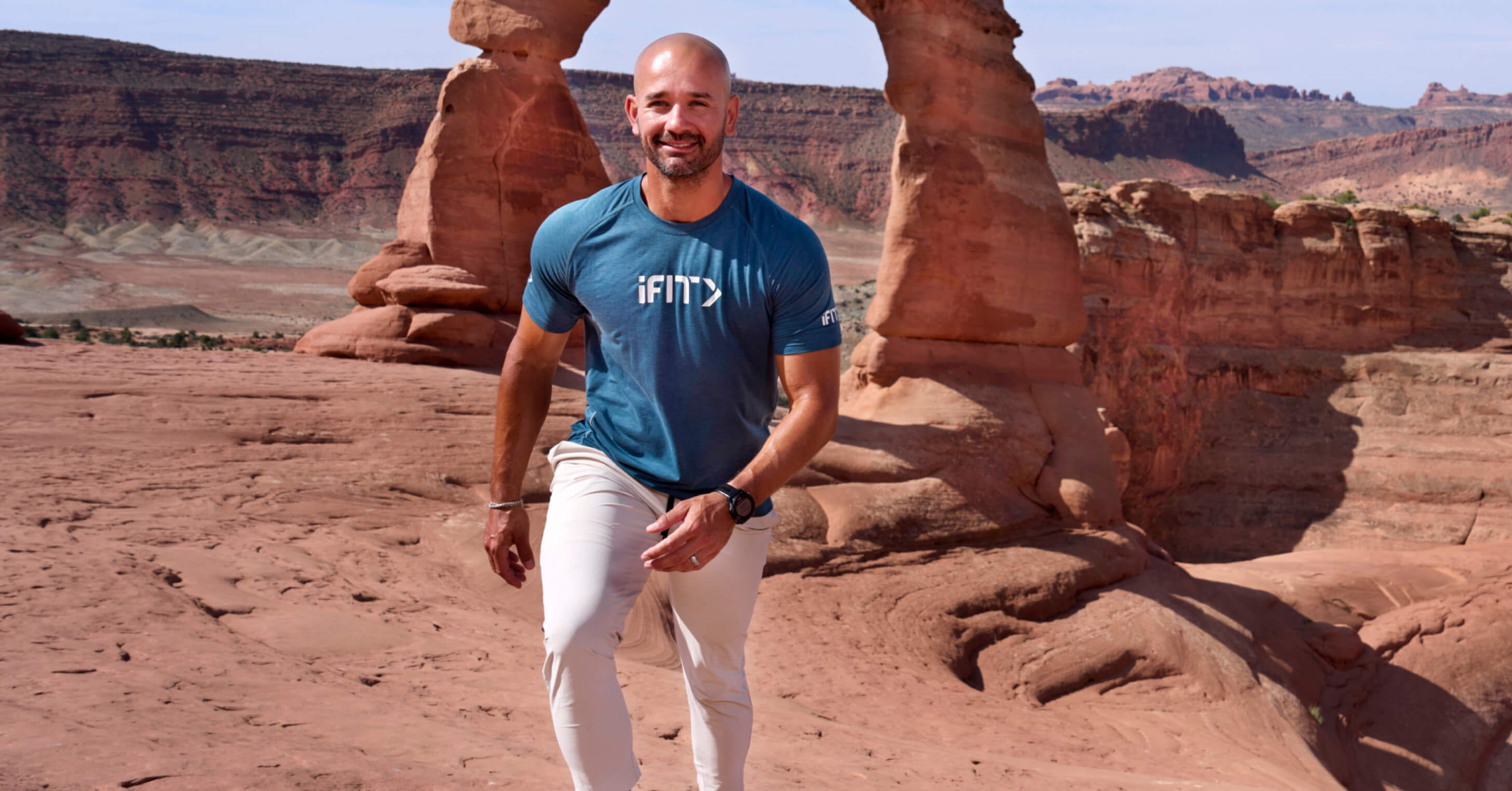 Explore Arches National Park on the iFIT app as Trainer Paulo Barreto walks beneath a sandstone arch.