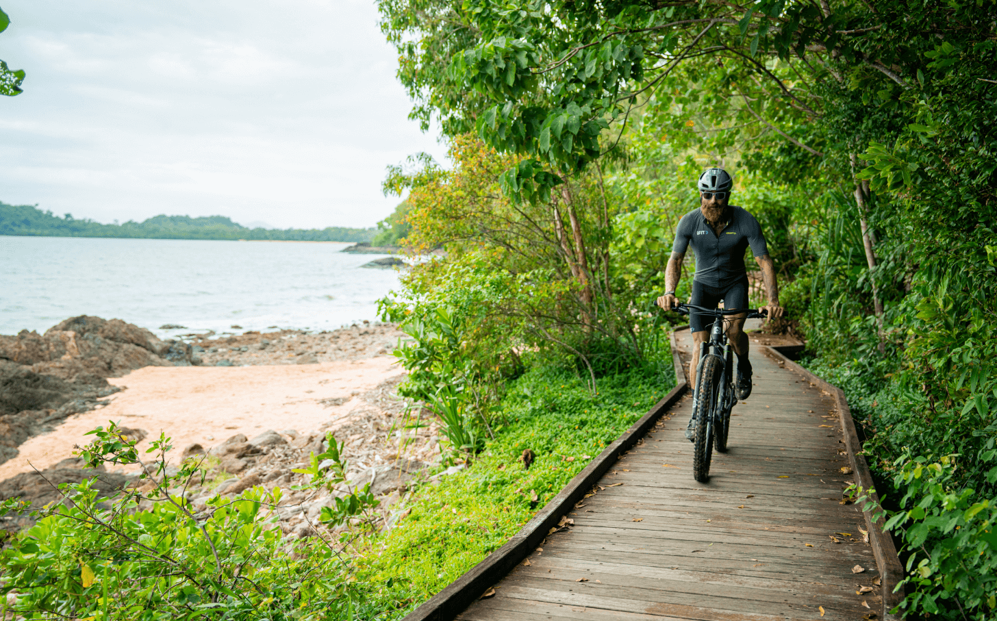 Tommy Rivs rides his bike on a forest boardwalk overlooking the coast.