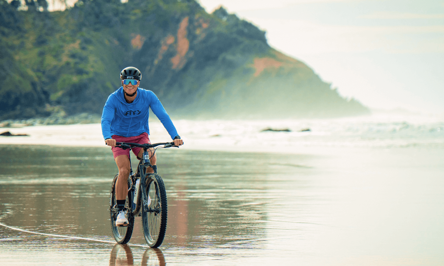 iFIT Trainer John Peel rides his bike along an Australian beach.