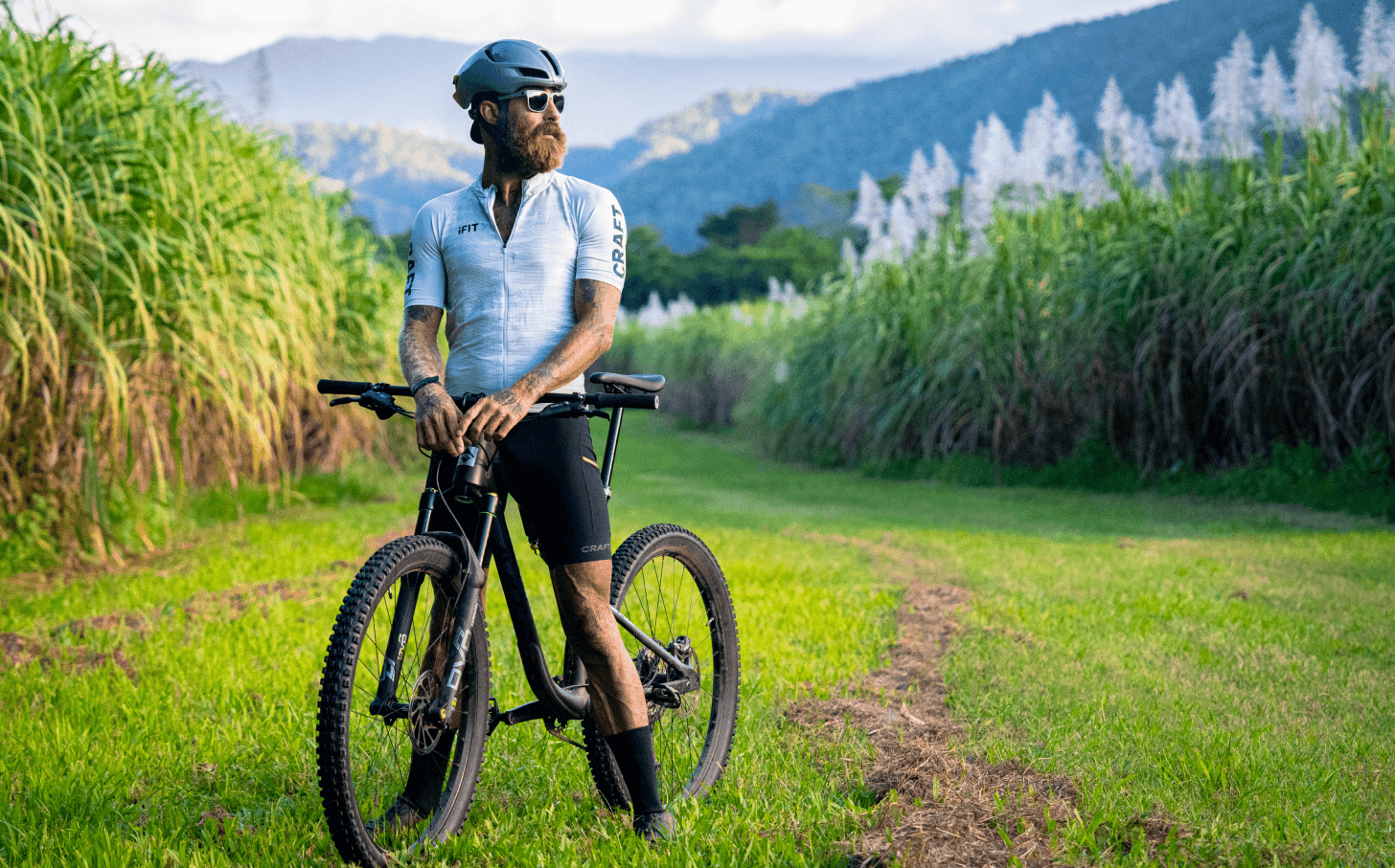 Tommy Rivs stands with his bike on a path between rows of crops.