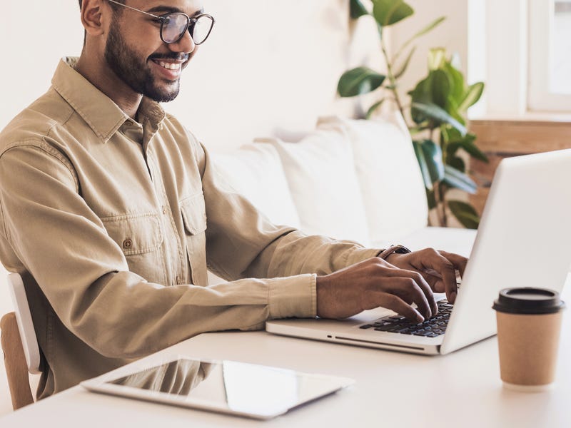 Ein junger Mann sitzt vor einem Laptop und schreibt.