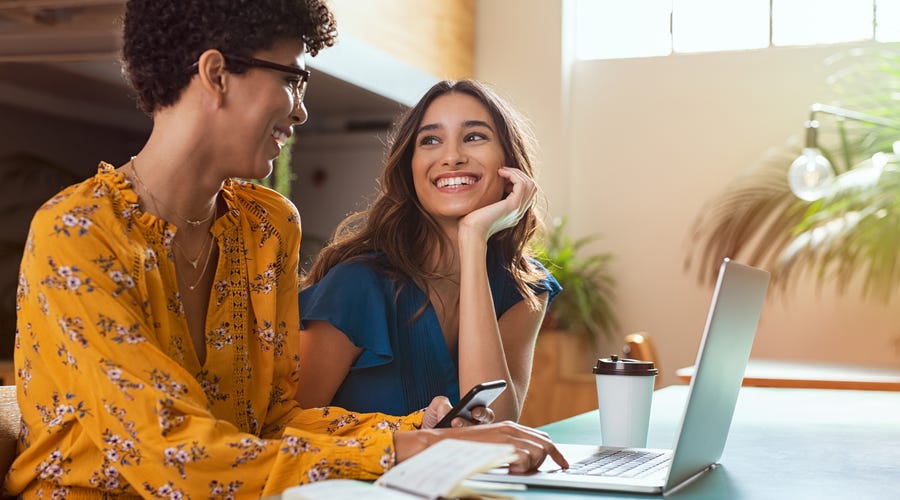 Two women sitting in front of a laptop and talking.