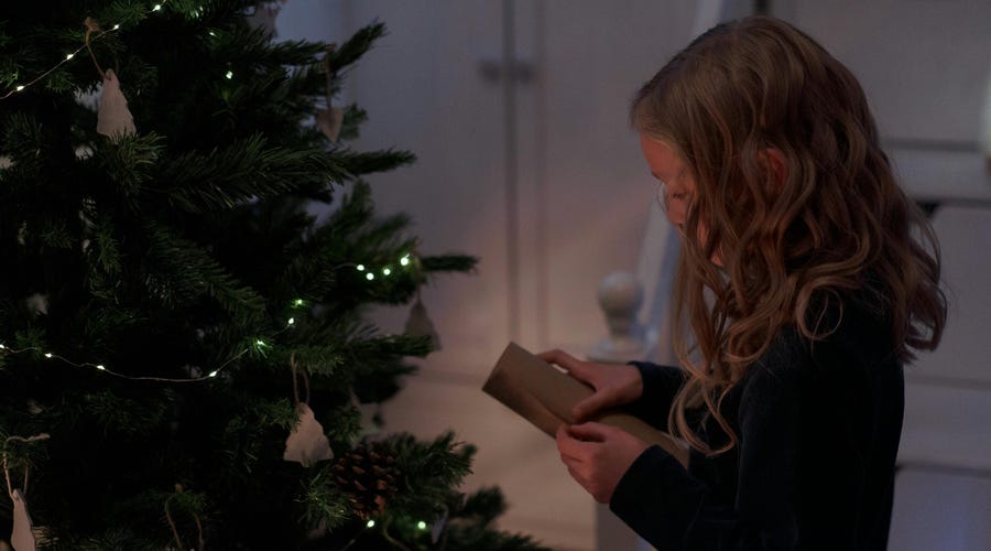 Kind rollt Brief am Tannenbaum aus.