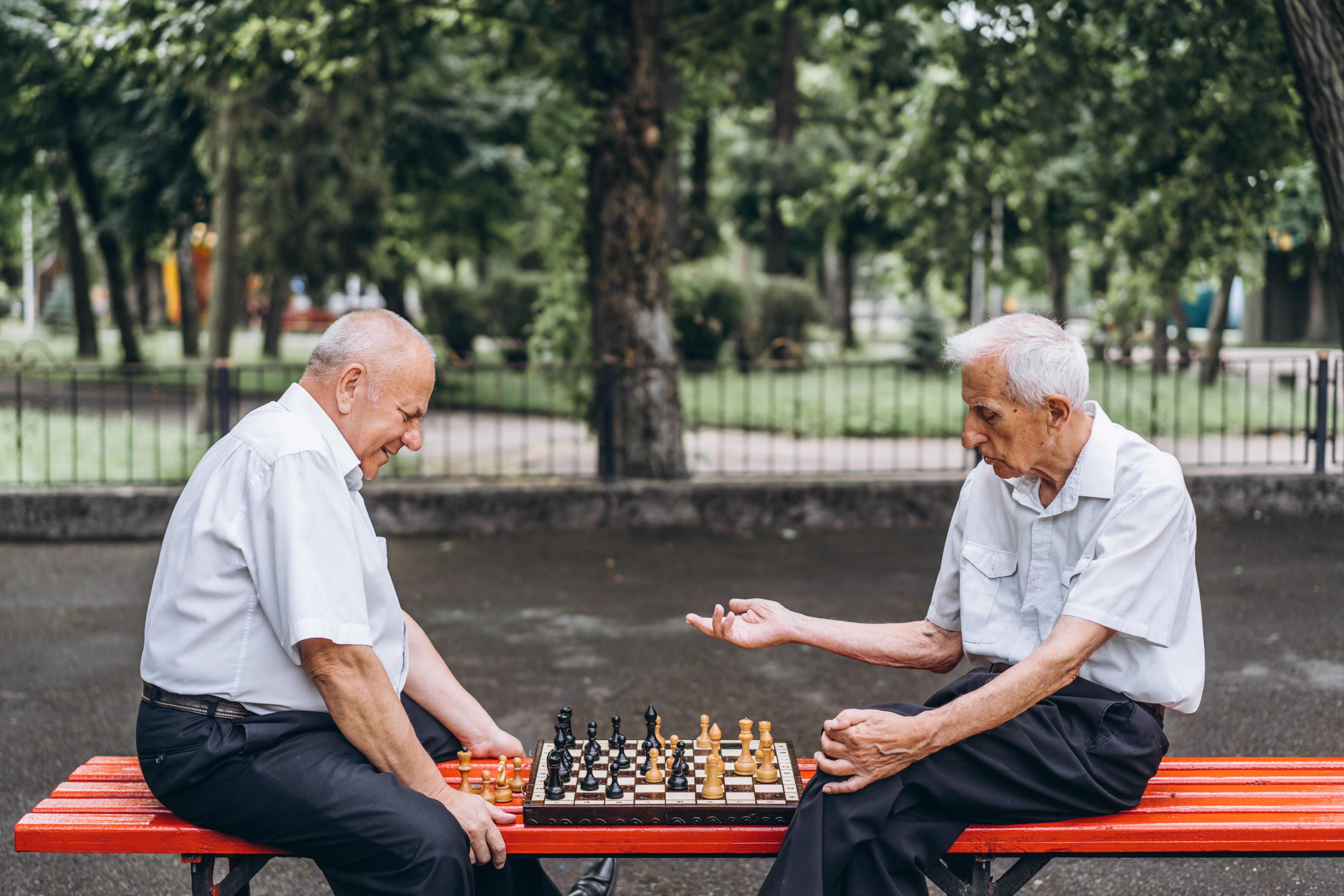 Zwei ältere Herren spielen draußen Schach.