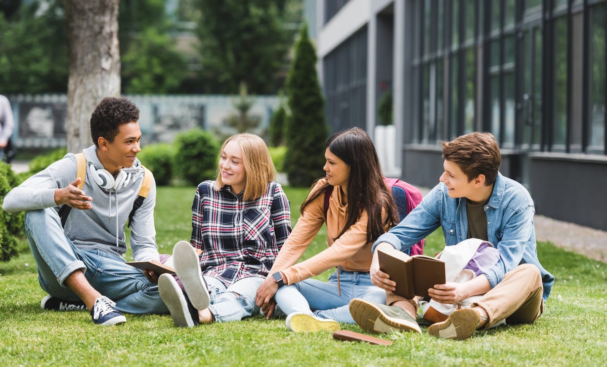 Mehrere Jugendliche sitzen draußen auf der Wiese und warten auf ihren Sprachkurs.