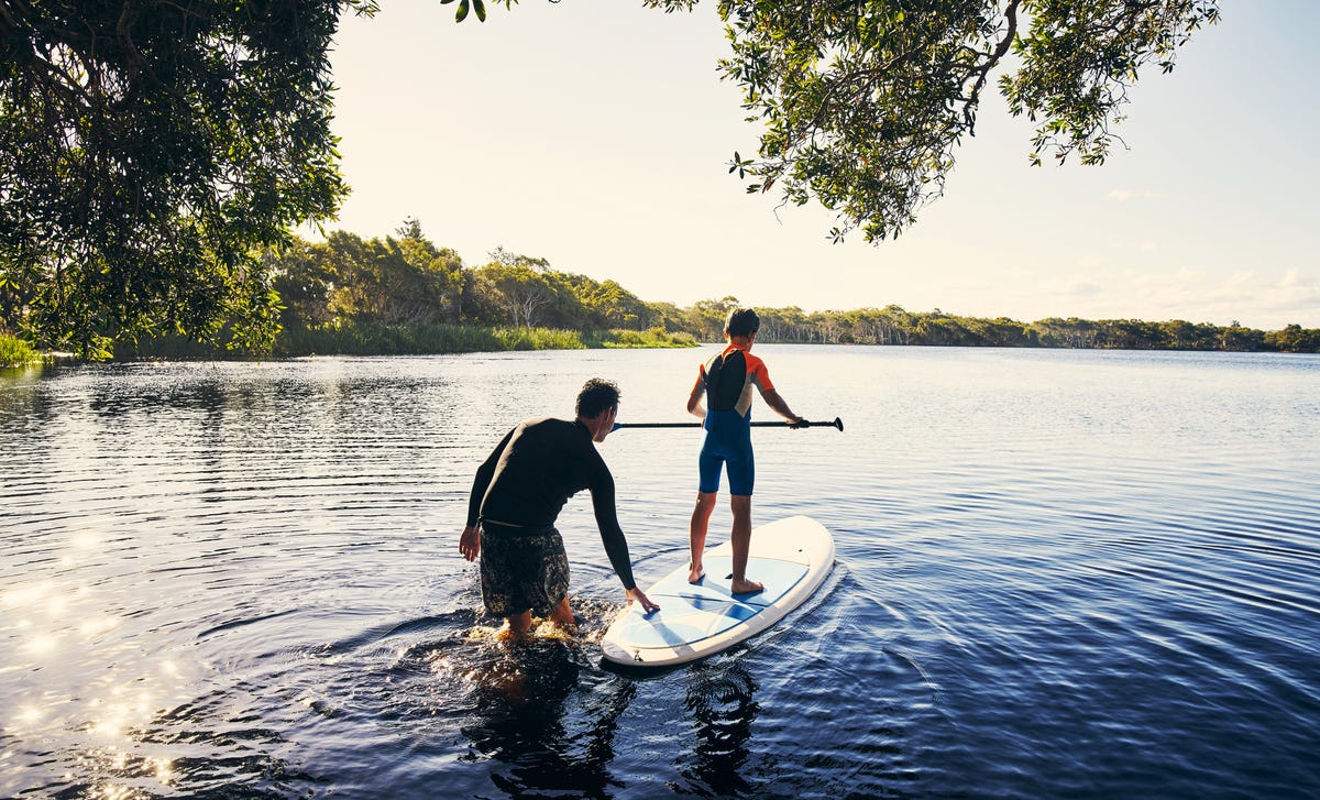 A man and a boy are getting onto a stand-up-paddle.