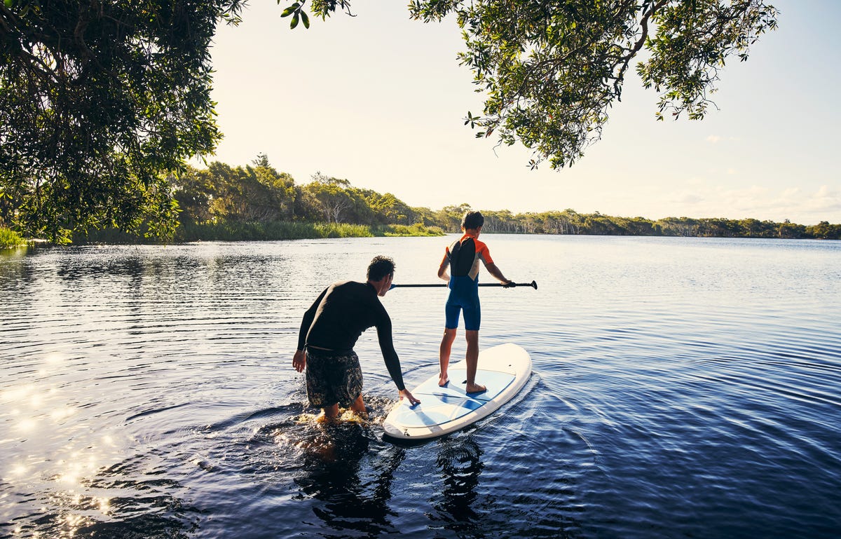 A man and a boy are getting onto a stand-up-paddle.