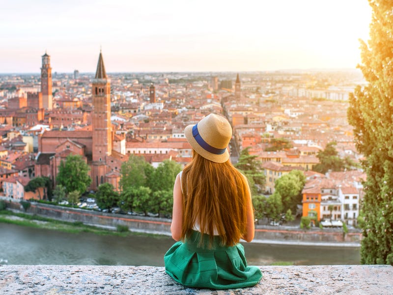 Frau sitzt auf Mauer und blickt Richtung Stadt