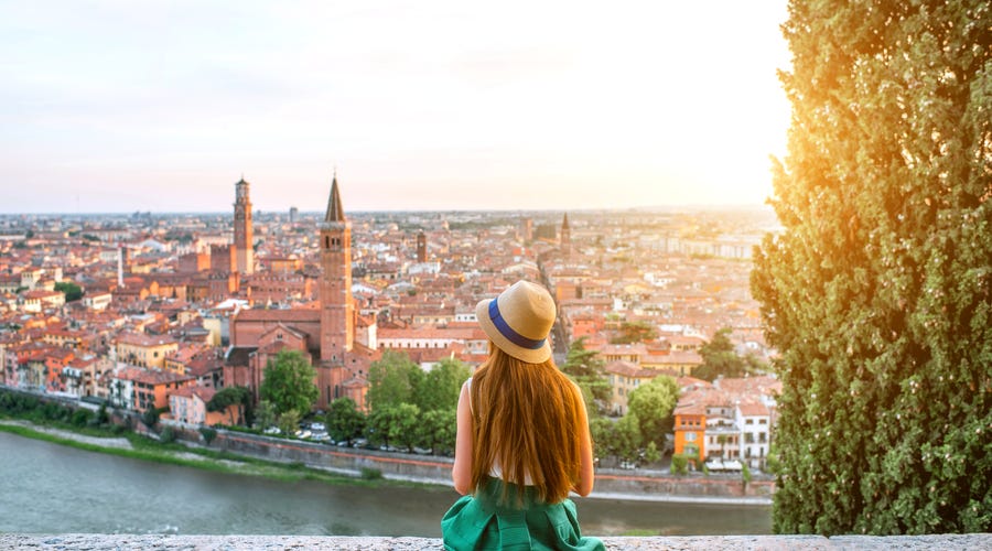 Frau sitzt auf Mauer und blickt Richtung Stadt