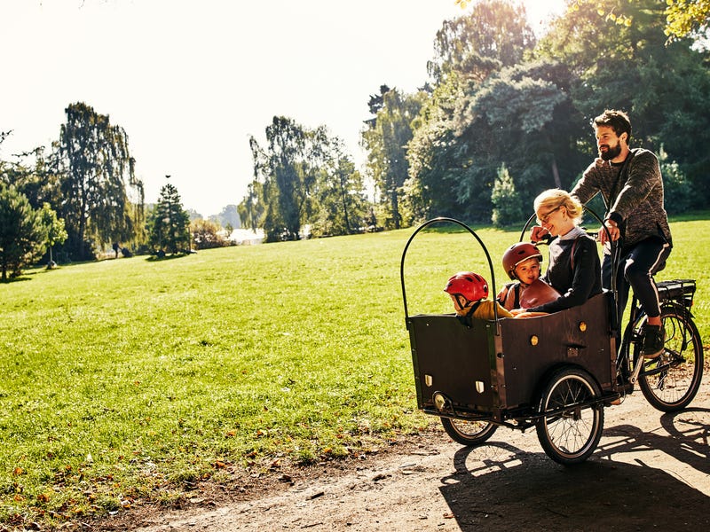 Vater fährt mit drei Kindern mit dem Lastenrad durch einen Park