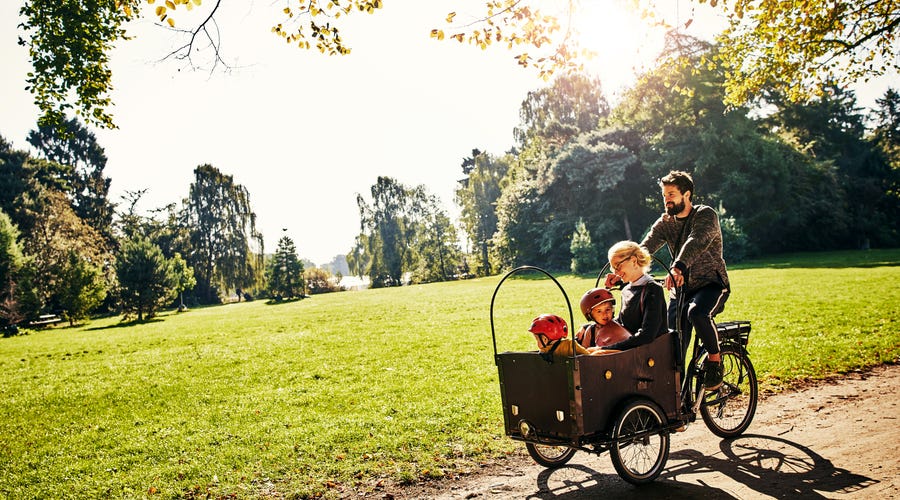 Vater fährt mit drei Kindern mit dem Lastenrad durch einen Park