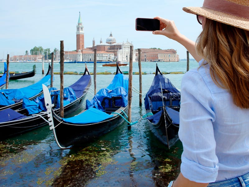 Eine Frau steht am Hafen und fotografiert Boote und Gebäude