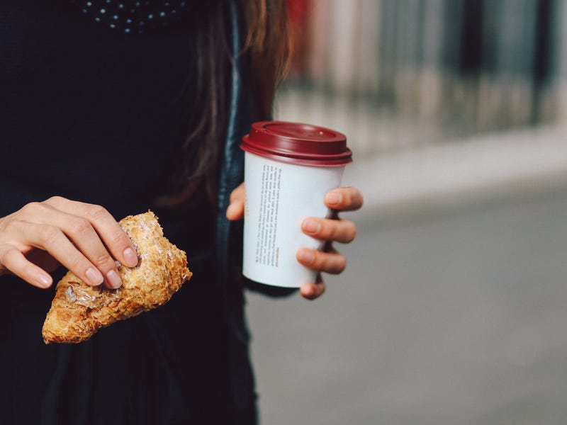 Frau hält Kaffee und Croissant in der Hand