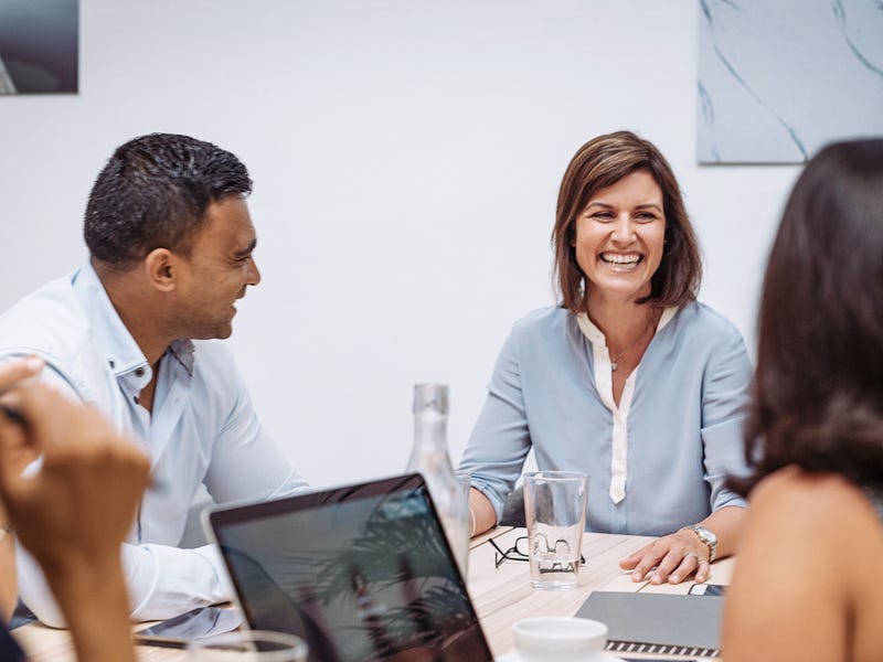 Mehrere Personen sitzen mit Laptop und Schreibmaterial an einem Tisch und sprechen.