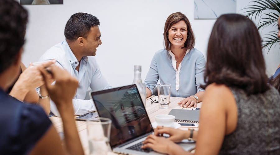 Mehrere Personen sitzen mit Laptop und Schreibmaterial an einem Tisch und sprechen.