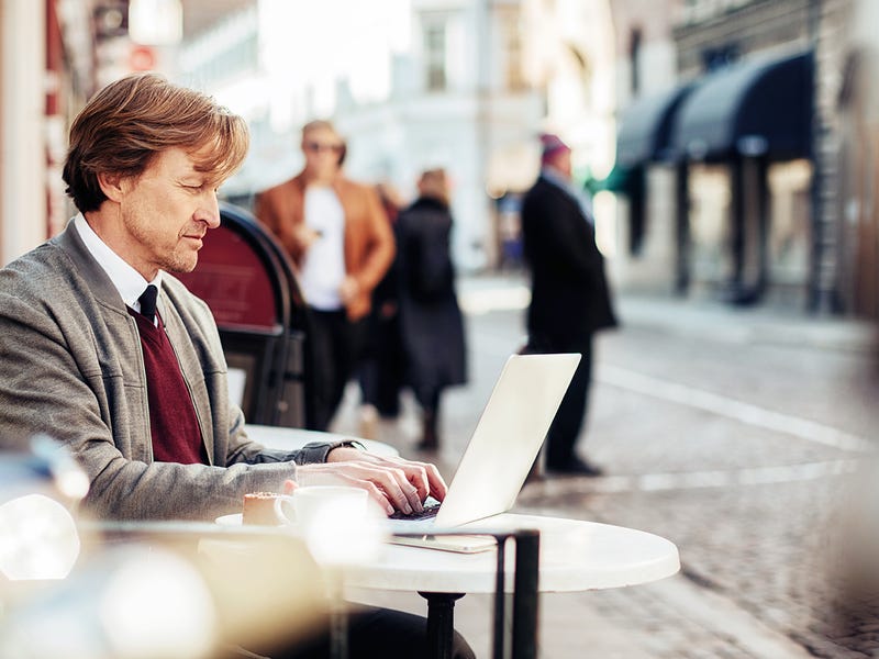 Mann sitzt in Café und arbeitet an seinem Laptop