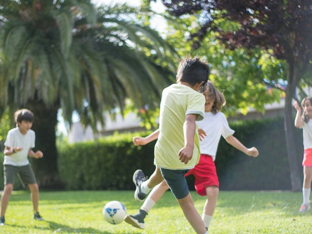 Kinder spielen in einem Sprachcamp Fußball auf der Wiese.