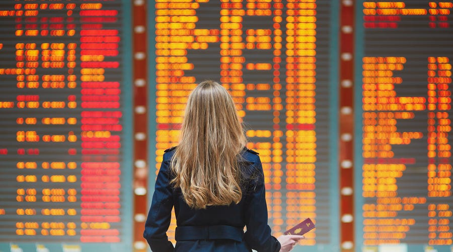 Frau steht am Flughafen vor Anzeigentafel.