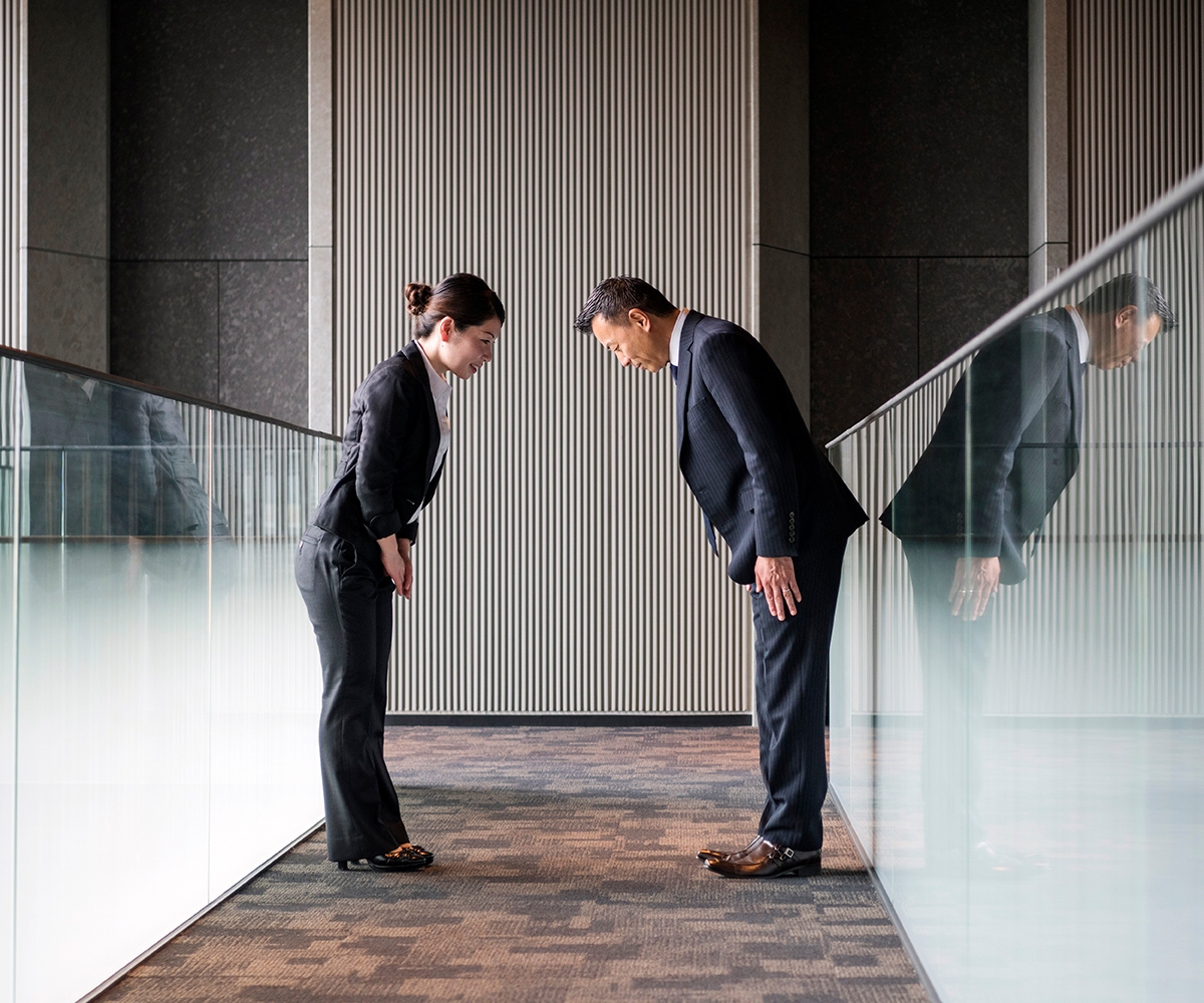 Ein Mann und eine Frau stehen sich gegenüber und begrüßen sich mit einer Verbeugung.