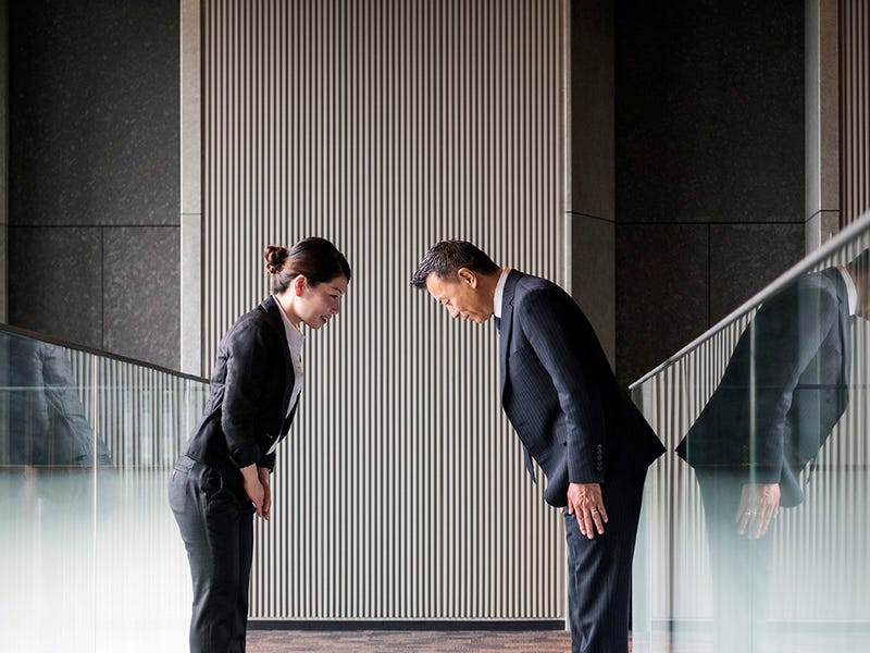 Ein Mann und eine Frau stehen sich gegenüber und begrüßen sich mit einer Verbeugung.