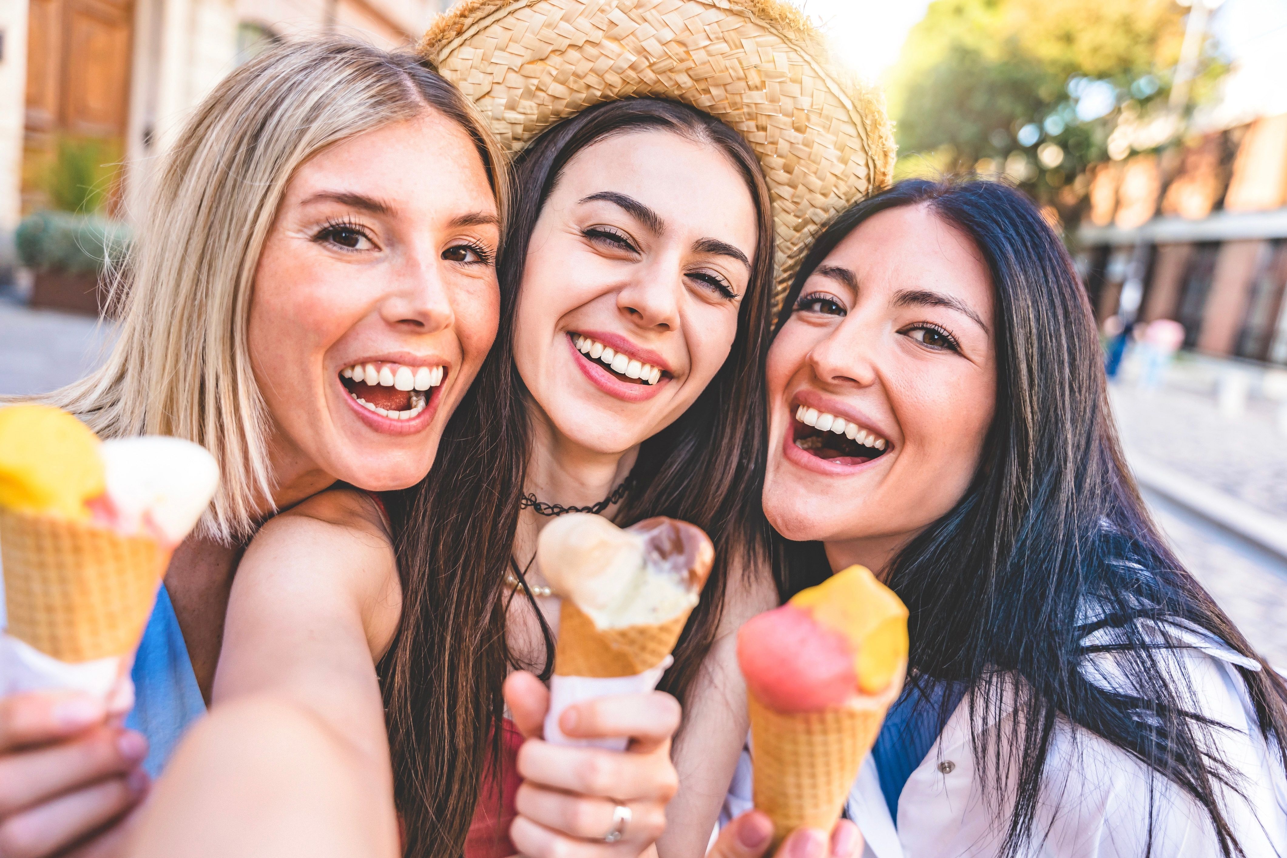 3 junge Frauen schauen lachend mit einem Eis in der Hand in die Kamera.