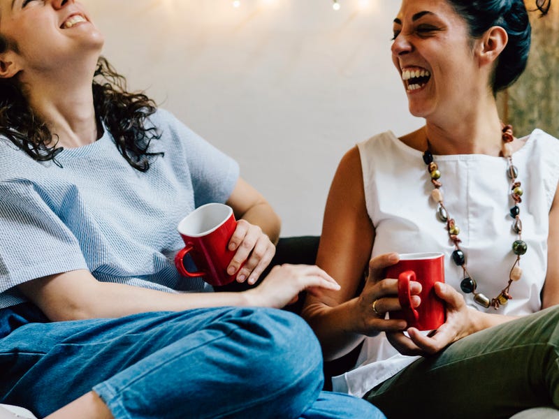 Zwei Frauen sitzen gemeinsam auf der Couch und lachen