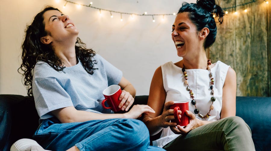 Zwei Frauen sitzen gemeinsam auf der Couch und lachen