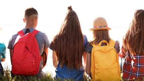 5 jugendliche Personen sitzen mit dem Rücken gekehrt zur Kamera auf Gras