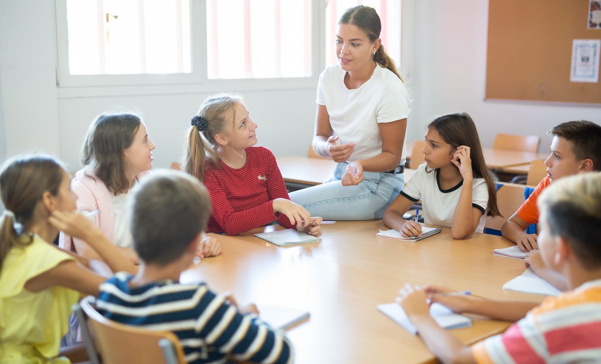 Mehrere Schüler sitzen im Sprachkurs mit ihrer Trainerin zusammen und reden über Aufgaben.