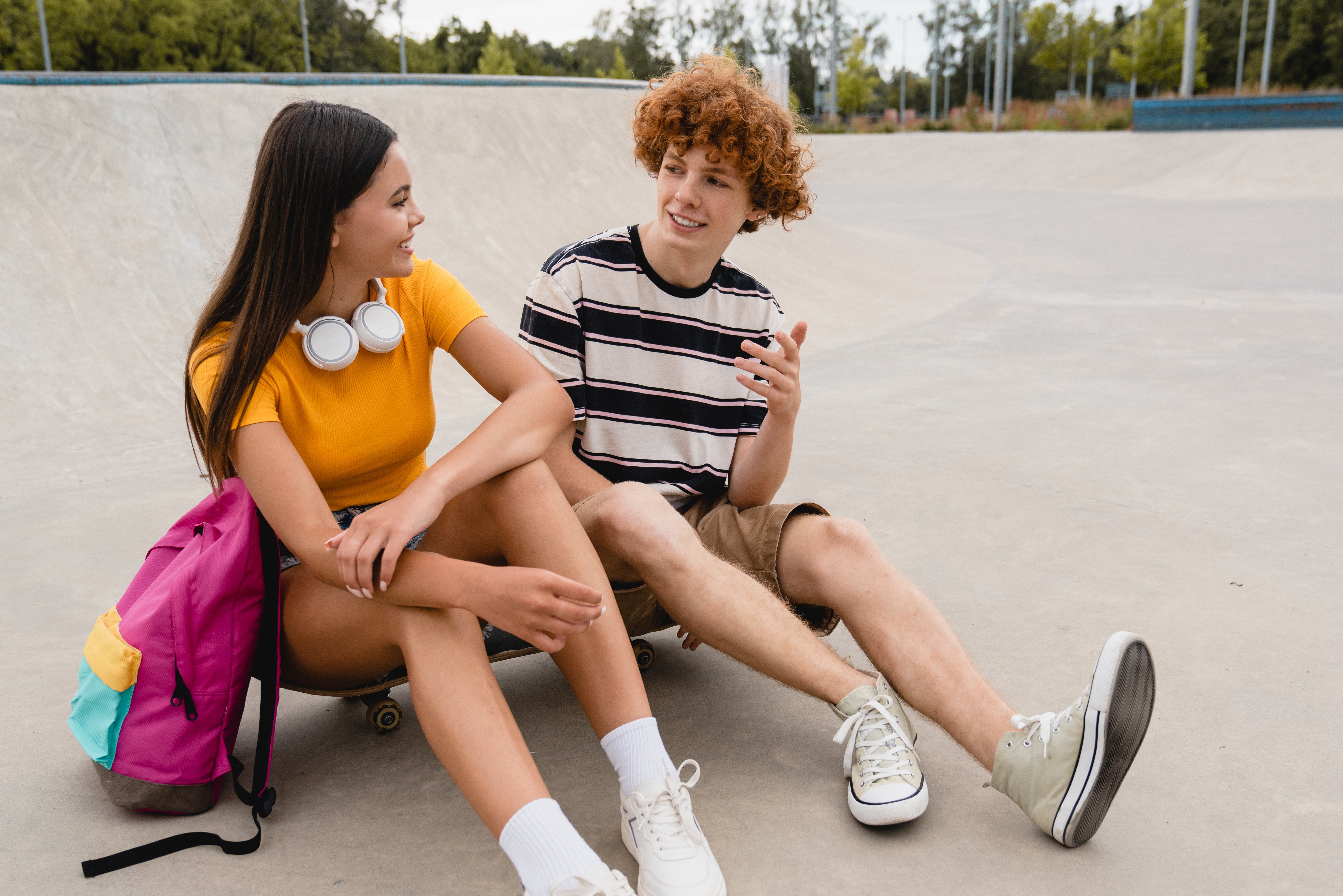 Zwei Jugendliche sitzen draußen im Skatepark zusammen und unterhalten sich über ihren Sprachkurs.