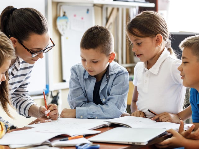Mehrere Kinder sitzen mit ihrer Trainerin zusammen und besprechen Aufgaben aus dem Sprachkurs.